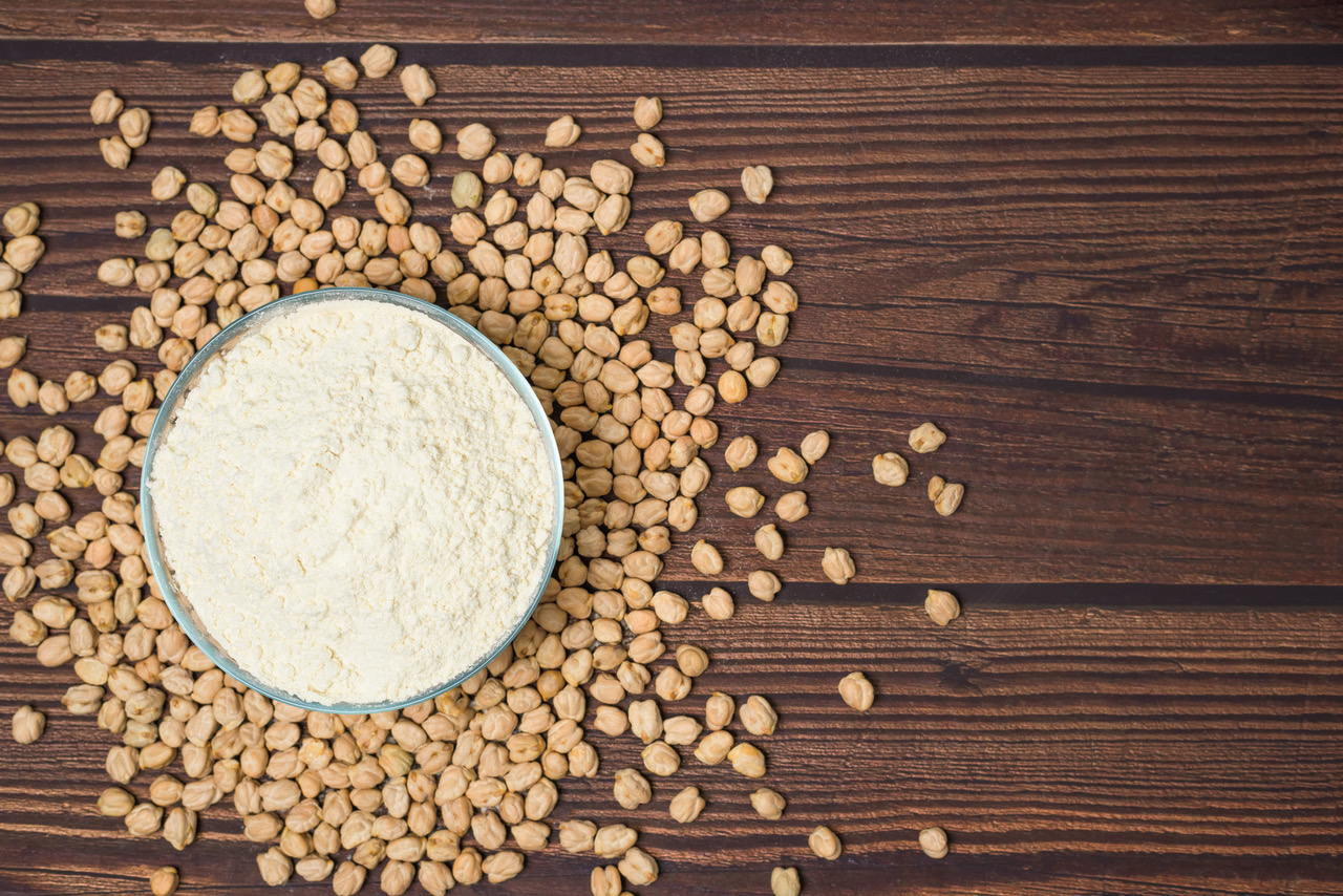 Photo of chickpea flour in a bowl with dried chickpeas surrounding it on a dark wood table background